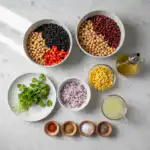 A vibrant array of fresh, colorful vegetables, herbs, and canned beans laid out, ready for a dense bean salad.